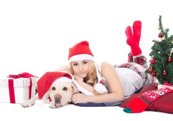 beautiful teenage girl in pajamas lying with dog in santa hat isolated on white background