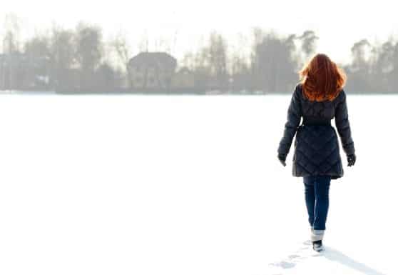 Pretty red haired girl walking on frozen lake and making footpath